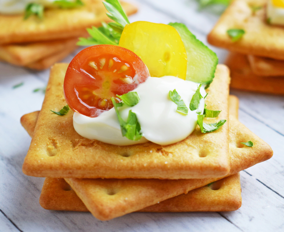 Three crackers topped with sour cream and vegetables.
