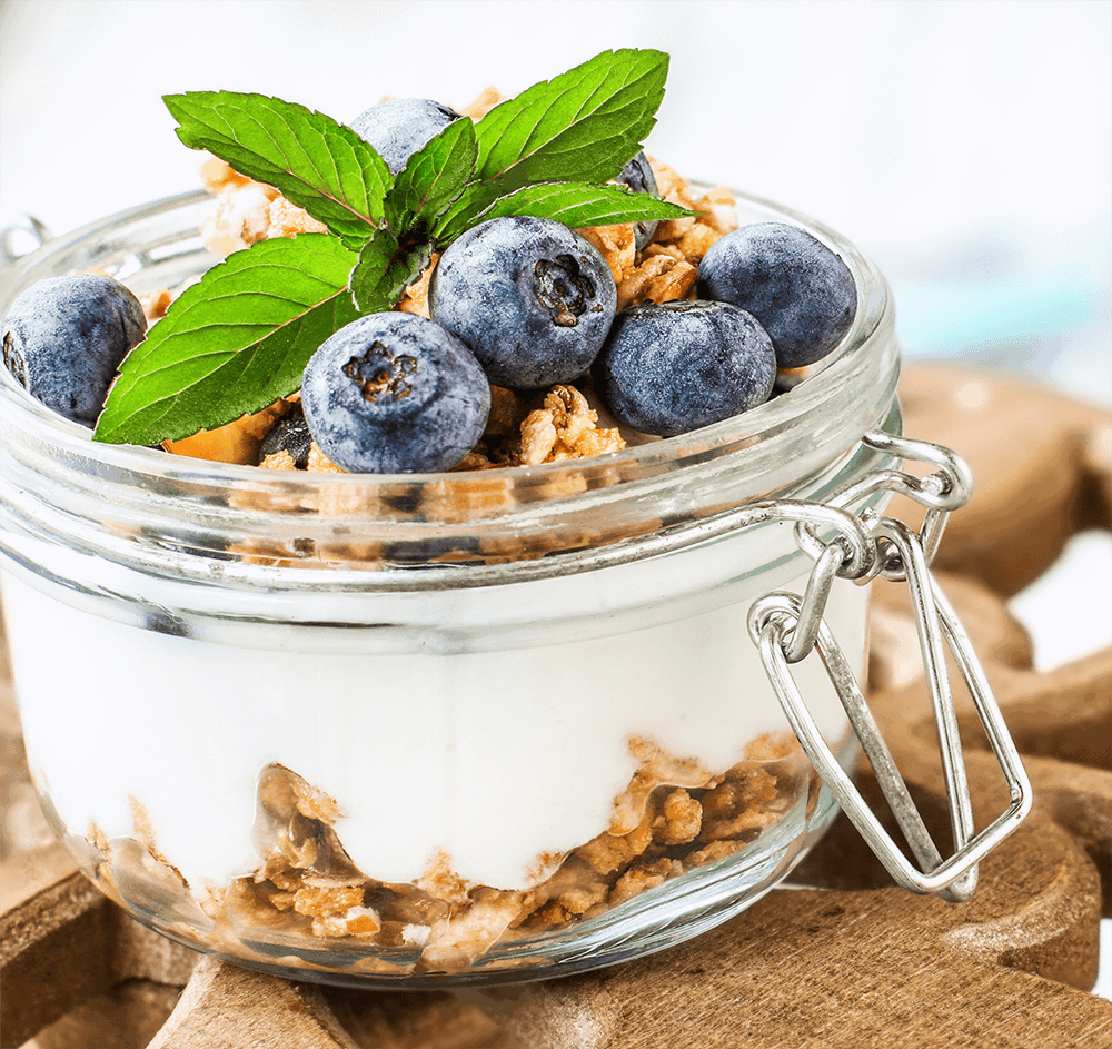 Yogurt in a glass jar layered with granola and blueberries and topped with mint.
