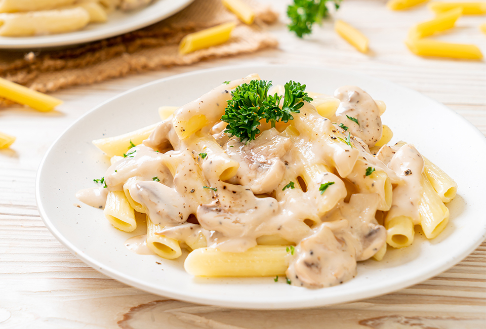 Penne pasta with white sauce and mushrooms topped with parsley.