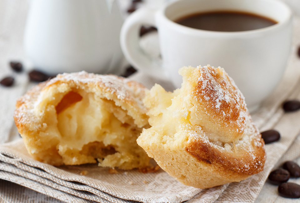 A sliced-open, cream-filled pastry beside a mug of coffee.