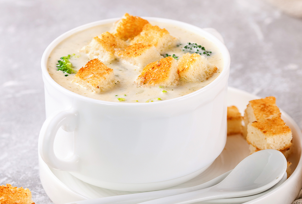 Creamy broccoli soup in a white mug topped with bread cubes.