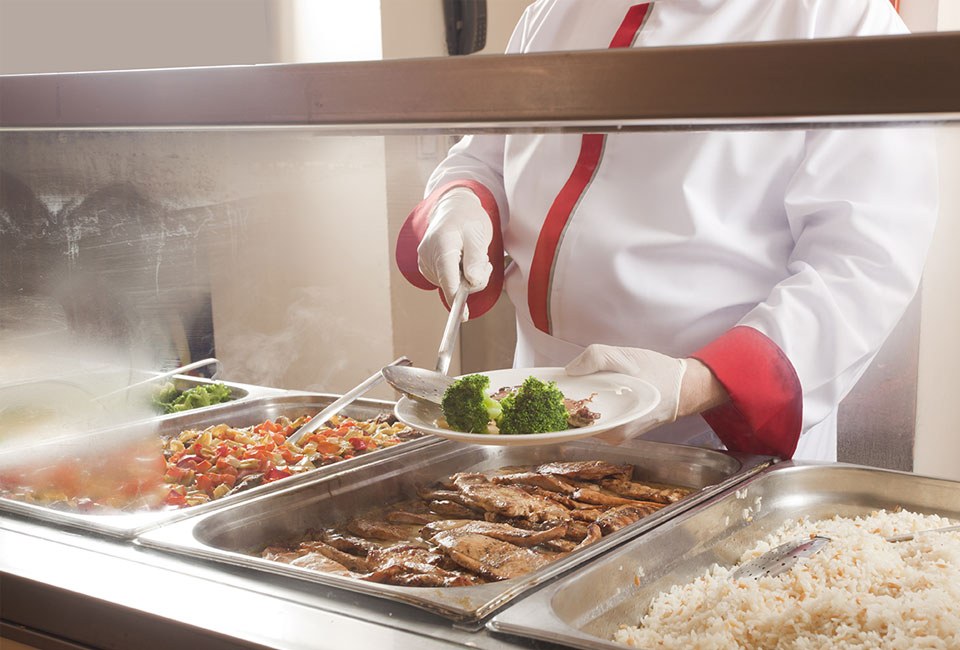 person serving meat and broccoli in buffet line