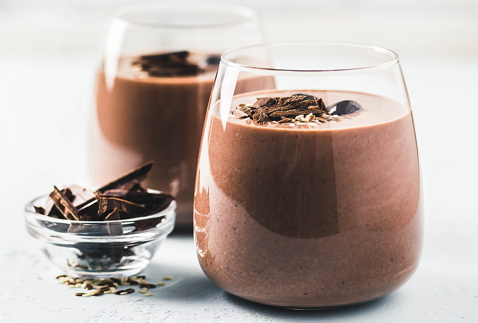 Chcoclate milk in clear glasses topped with chocolate shavings beside a glass bowl of additional chocolate shavings.