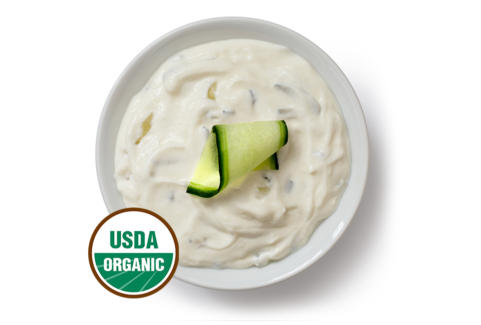Arial view of creamy dip in a white bowl topped with a cucumber slice with a USDA organic logo.