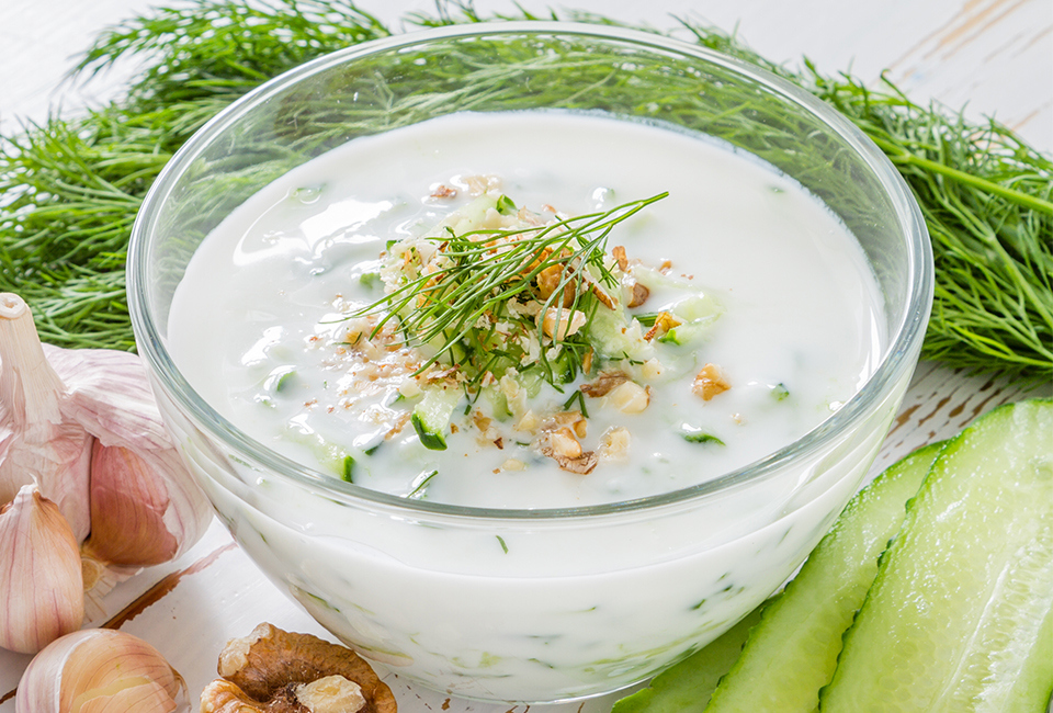 Creamy dip in clear bowl topped with cucumber pieces, walnut pieces and dill.