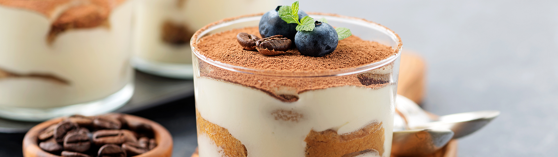 Layered parfait topped with blueberries, coffee beans and mint beside a small bowl of coffee beans.