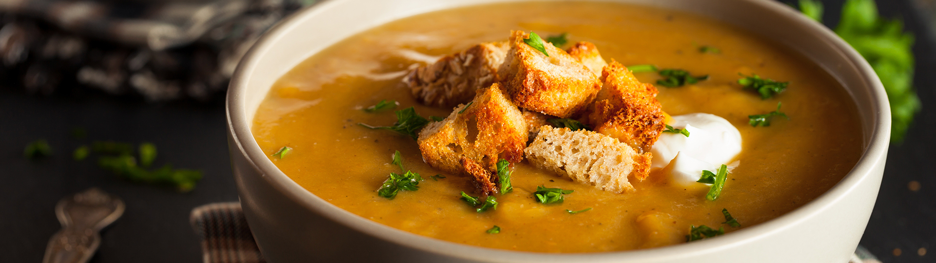 Orange bisque-style soup in grey bowl topped with herbs, croutons and cream.